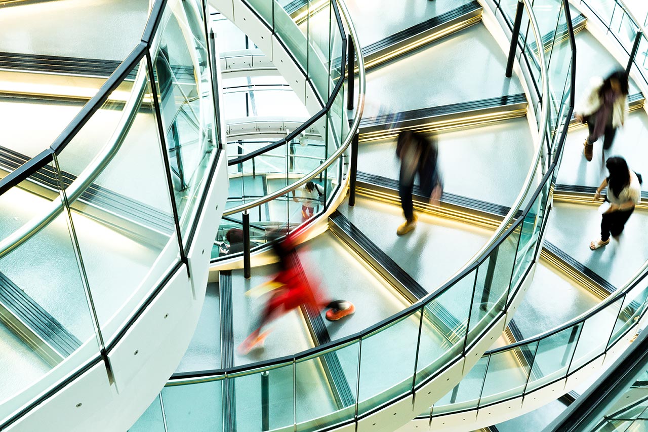 Betriebliche Altersvorsorge für Unternehmen Verschwommene Menschen auf spiralförmigen Treppen symbolisieren Dynamik im Unternehmenskontext